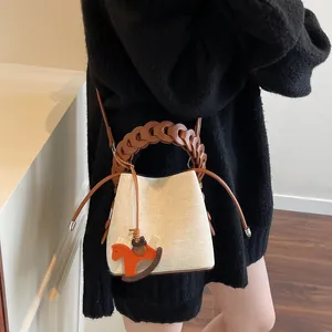 Detail of cream woven bucket bag with brown ring handle and orange horse charm accessory