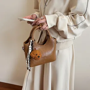Dettaglio borsa vintage in pelle marrone con ciondolo di peluche e logo in rilievo