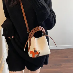 Detail of canvas bucket bag with leather trim, woven handle and a wooden horse charm