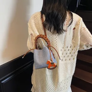 Blue denim bucket bag with brown woven handle and horse charm shown on model