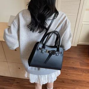 Sac fourre-tout en cuir noir avec boucle dorée porté par un mannequin pour un style chic