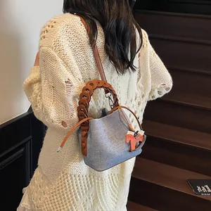 Close-up of a blue bucket bag with woven texture, leather handle and horse charm on a model