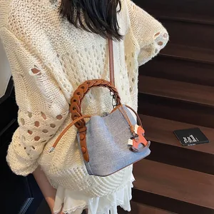 Detail of light blue textured bucket bag with woven handle and orange horse charm