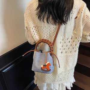 Detail of light blue fabric bucket bag with woven handle and small horse charm accessory
