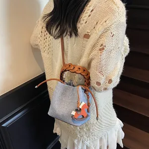 Detail of light blue bucket bag with woven handle and orange horse charm on a model