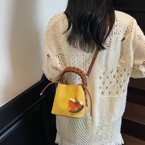 Woven bucket bag in yellow with brown leather handles and a horse charm on model