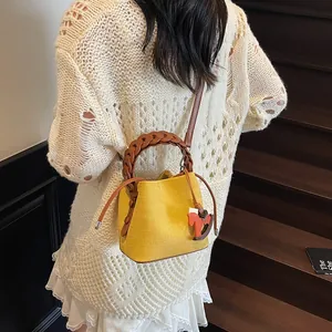 Detail of yellow canvas bucket bag featuring a braided brown handle and a cute horse charm