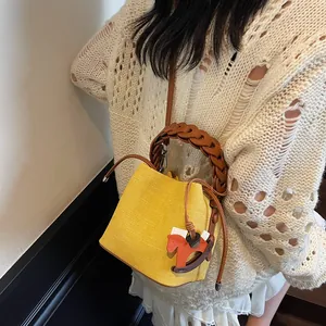 Detail of yellow bucket bag with woven handle and horse charm on knit outfit