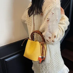 Close-up of a yellow bucket bag with woven leather handles and a horse charm detail