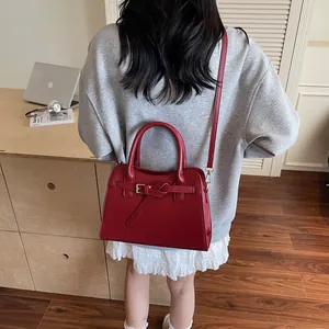 Sac à main trapèze rouge foncé avec nœud à boucle dorée porté dans un décor de bureau