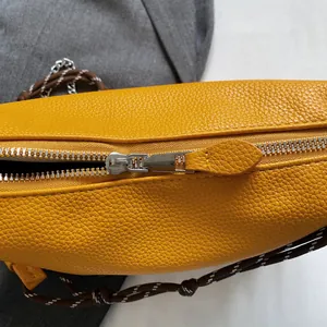 Detail of silver metal zipper and yellow lychee grain leather texture on a shoulder bag