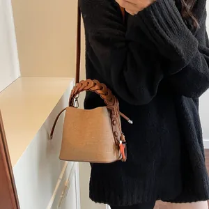 Detail of a beige canvas bucket bag with woven leather handles and drawstring closure