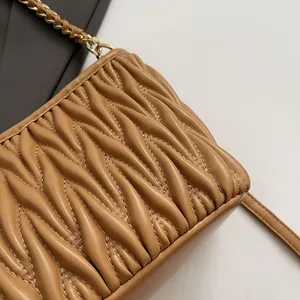 Détail macro du sac seau matelassé chameau avec bandoulière chaîne dorée chic