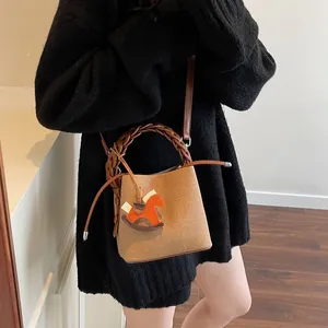 Detail of woven bucket bag with leather trim and decorative orange rocking horse charm