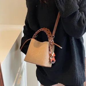 Close-up of beige canvas and brown leather bucket bag with braided handle and horse charm