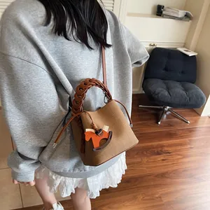Detailed view of brown bucket bag featuring woven handle and wooden rocking horse charm