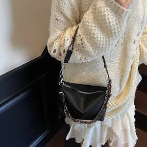 Close-up of black pebble leather moon bag with woven strap and silver chain on beige sweater
