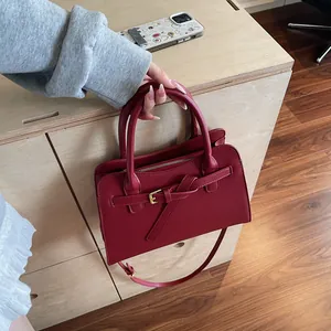 Détail d'un sac cabas bordeaux avec boucle en métal doré et bandoulière sur comptoir