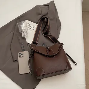 Vue à plat d'un sac seau en cuir grainé marron sur costume gris avec bandoulière