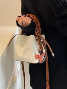 Mini canvas bucket bag with brown woven handle and leather trim against a minimal wall