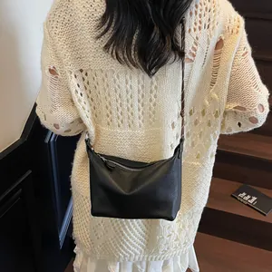 Detail view of black lychee grain leather crossbody bag with silver zipper and strap