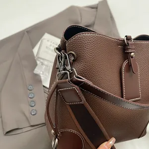 Détail d'un sac seau en cuir marron foncé avec surpiqûres et bandoulière rayée