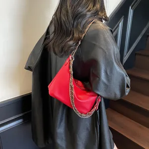Detail of red hobo bag with lychee texture and woven metal chain strap against black leather
