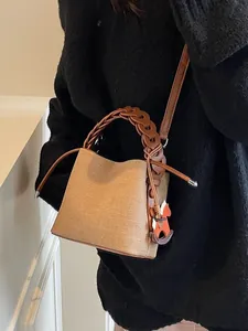 Straw-textured bucket bag with woven leather handle and rocking horse charm on a model