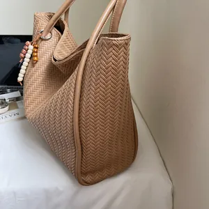 Detail of khaki woven tote bag with handle and colorful beaded charm on a white desk