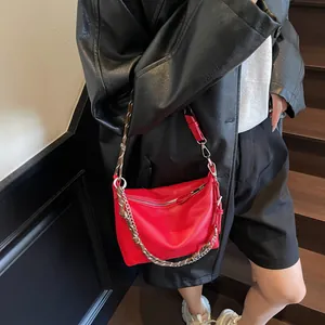 Detail of red textured shoulder bag with woven strap and silver chain on model