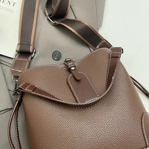 Détail du sac seau en cuir grainé marron avec bandoulière large en tissu rayé