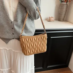 Détail du sac seau matelassé caramel avec bandoulière en chaîne dorée et cuir tissé
