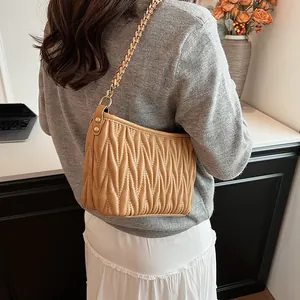 Détail du sac seau kaki clair avec texture plissée et bandoulière chaîne sur modèle