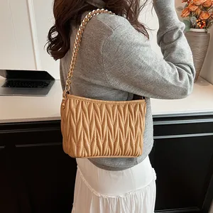 Détail d'un sac seau plissé marron clair avec chaîne dorée sur un mannequin femme