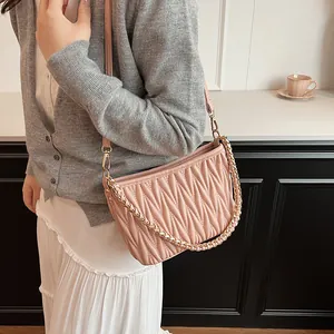 Détail du sac seau plissé rose clair avec une poignée élégante en chaîne à maillons dorés