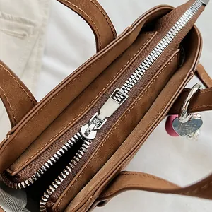 Dettaglio macro della borsa in pelle marrone con zip argento e ciondolo a cuore