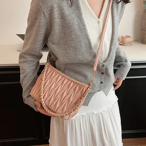 Sac seau rose plissé porté en bandoulière par un mannequin avec chaîne dorée et cuir