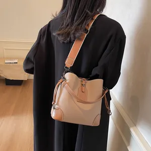 Sac seau en cuir marron avec large bandoulière en textile porté par un mannequin chic