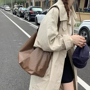 Detailed view of dark brown woven tote bag with wide shoulder strap in street setting