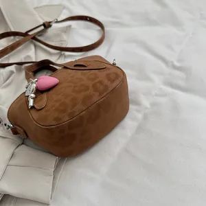 Dettaglio borsa leopardata in pelle scamosciata con ciondolo a cuore rosa su sfondo trench