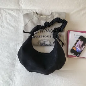 Flat lay of black hobo bag with pleated handle on white fabric with outfit accessories