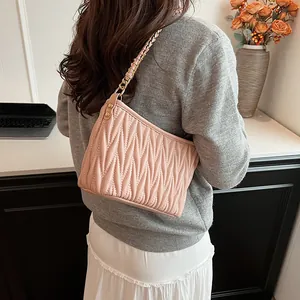 Détail d'un sac seau rose plissé avec bandoulière chaîne dorée porté par un mannequin
