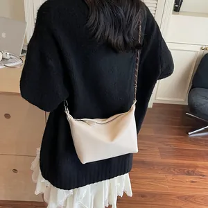 Detail of a creamy white pebbled leather crossbody bag with silver chain strap shown on a model