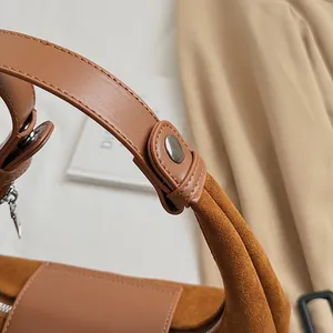 Detailed close-up of brown suede and leather texture with silver metal buckle on handbag