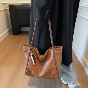 Close-up of a large dark brown woven leather tote bag with stylish beaded accessory