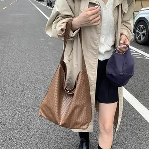 Outdoor street view of a large brown woven leather tote bag paired with a beige trench coat