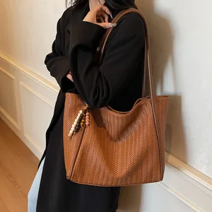 Detail of brown woven tote bag with V-shaped texture and decorative beaded tassels