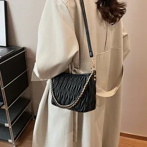 Détail d'un sac seau noir plissé avec chaîne dorée porté par un mannequin à l'épaule