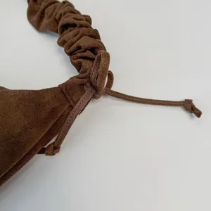 Detail of dark brown suede handbag featuring drawstring knots and ruched handle texture