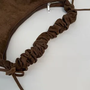Close-up of dark brown suede crossbody bag with pleated strap and silver zipper detail